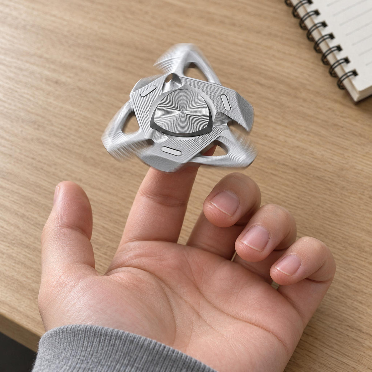 Hand holding silver metal shark fin fidget toy over office desk workspace