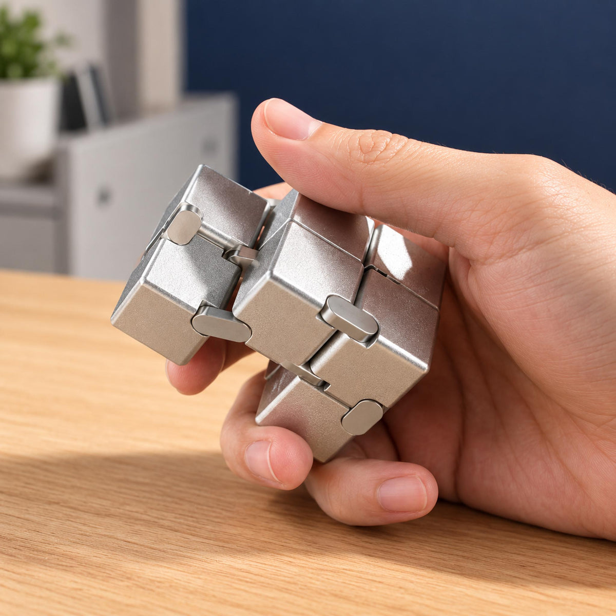 Adult hand folding silver metal infinity cube fidget toy at wooden office desk